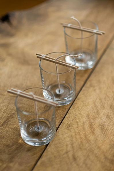 Empty glass candle jars with wicks placed in them being held up by sticks.